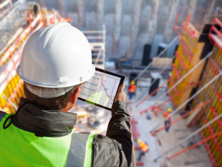 civil engineer or architect with hardhat on construction site checking schedule on tablet computer