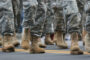 Military service members march on a road. Only boots and lower legs visible