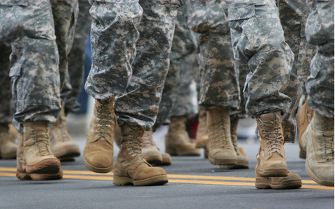 Military service members march on a road. Only boots and lower legs visible